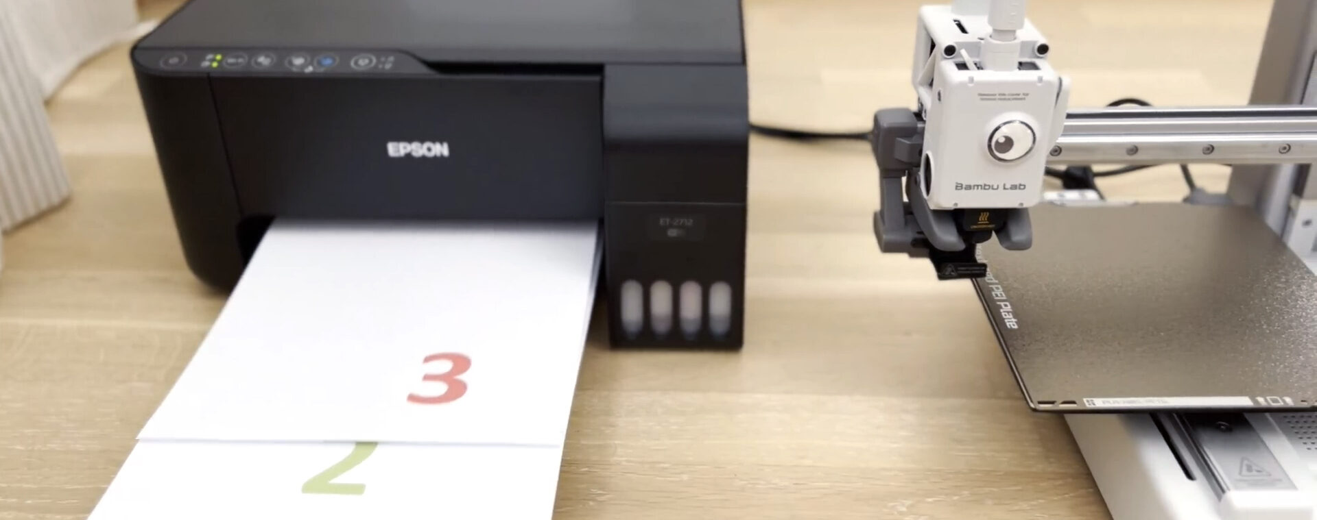 BambuLab A1 mini 3D printer is shown next to a classic paper printer, which is printing multiple pages